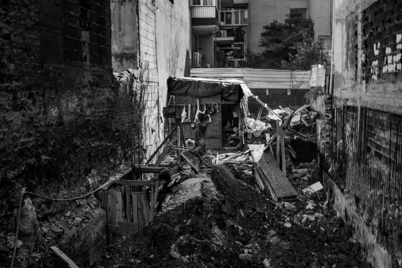 A worker in a narrow construction site between buildings, in black and white