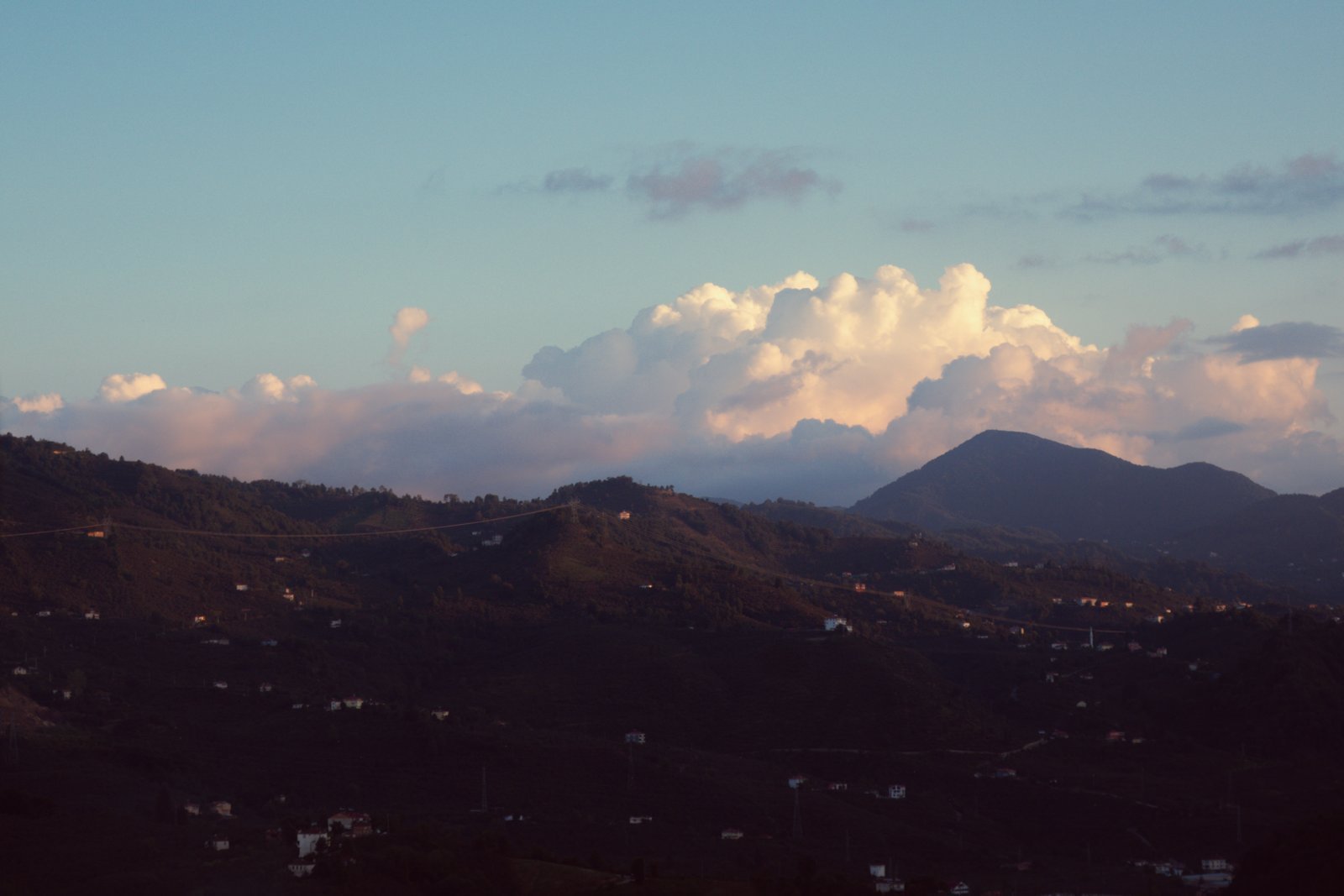 Towering clouds over green hills and scattered houses at dusk