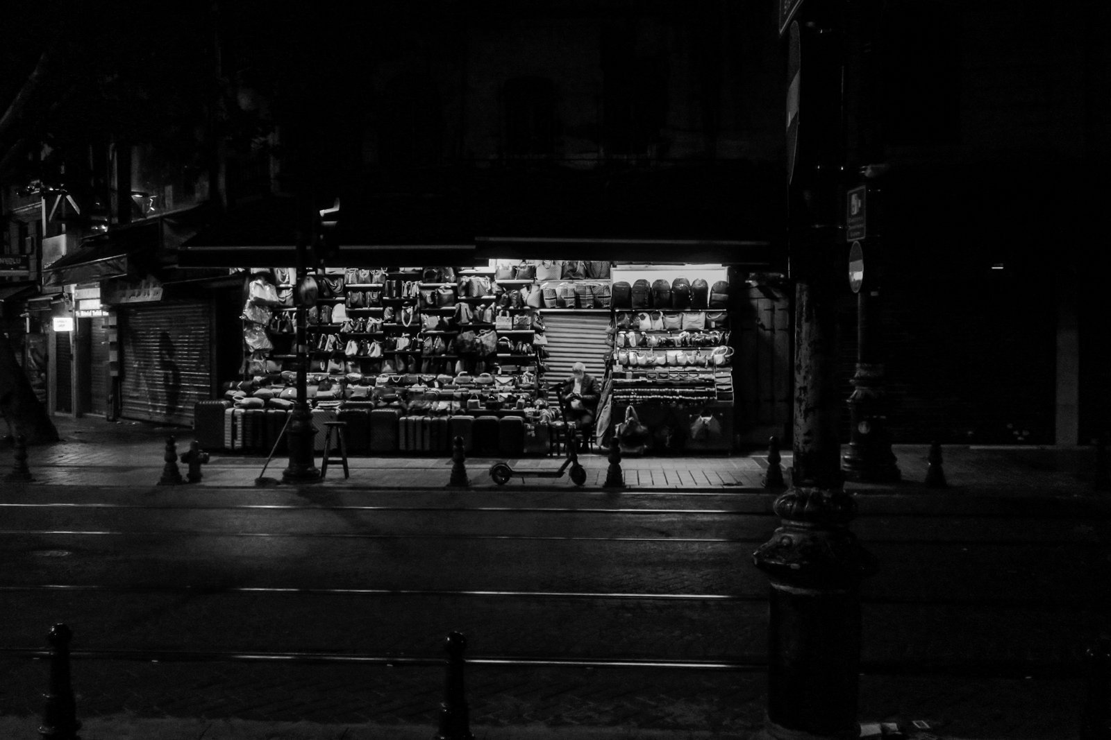 A lit-up bag stall on a dark street at night, in black and white